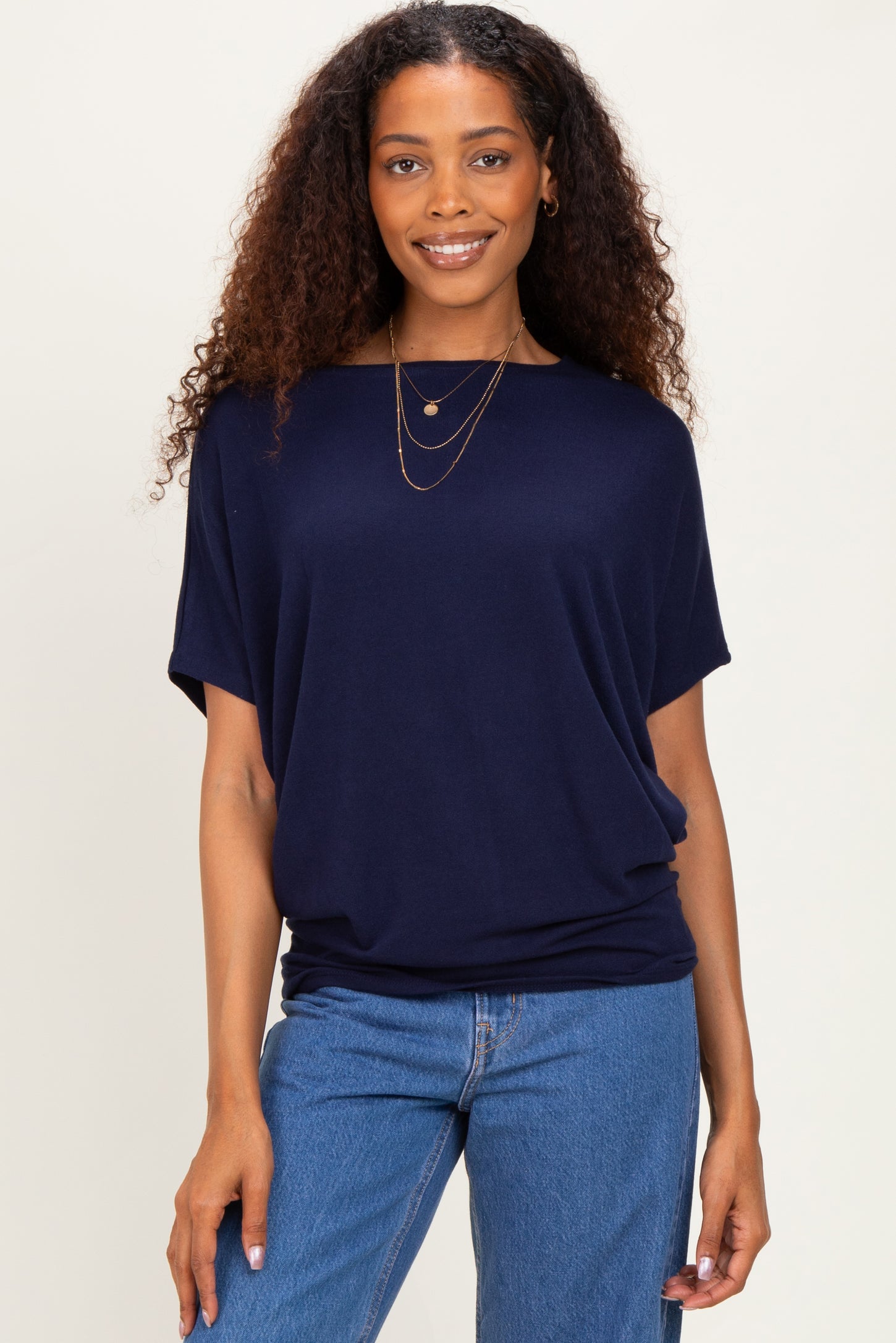woman wearing a navy blue short sleeve top with relaxed fit and layered necklaces, paired with blue jeans