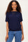 woman wearing a navy blue short sleeve top with relaxed fit and layered necklaces, paired with blue jeans