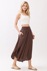 woman wearing a brown smocked waist maxi skirt and a white crop top, posing with one hand in the pocket