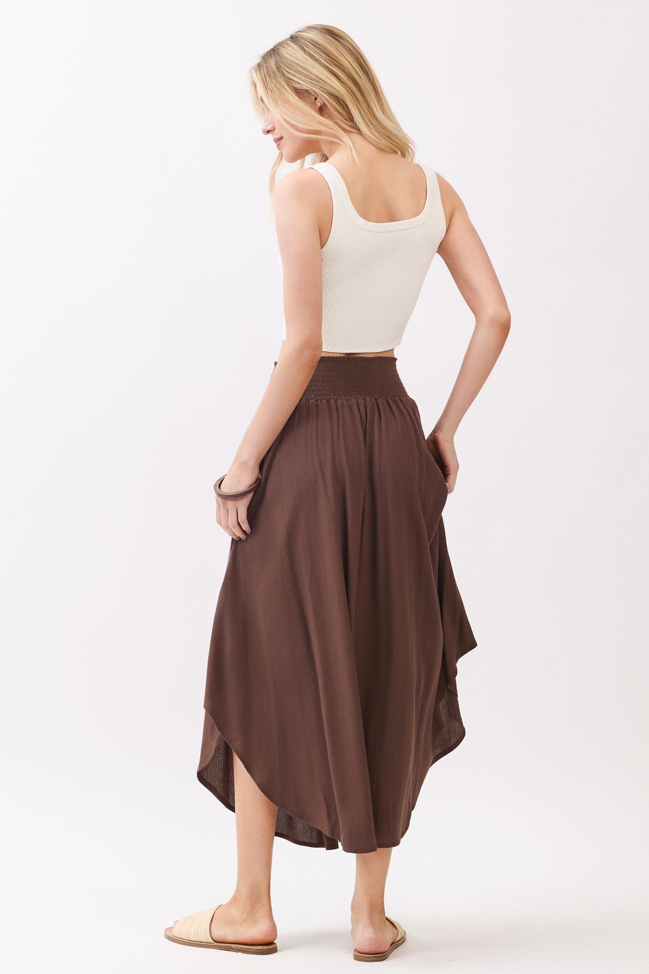 woman wearing a white ribbed crop top and a brown high-low midi skirt, showing the back view and styled with sandals