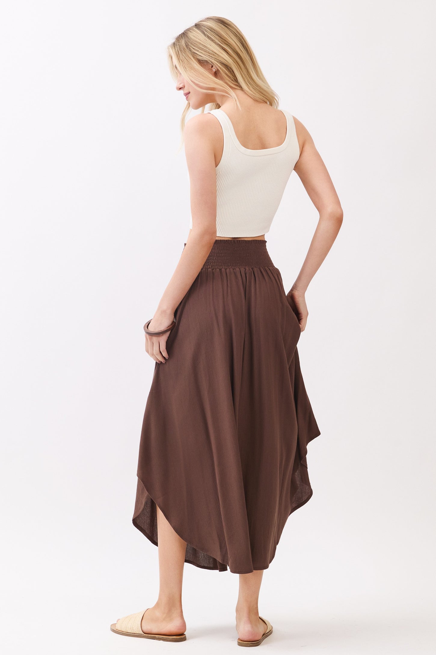 woman wearing a white ribbed crop top and a brown high-low midi skirt, showing the back view and styled with sandals