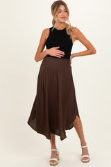 woman wearing a black sleeveless top and a brown asymmetrical maternity skirt, holding her baby bump