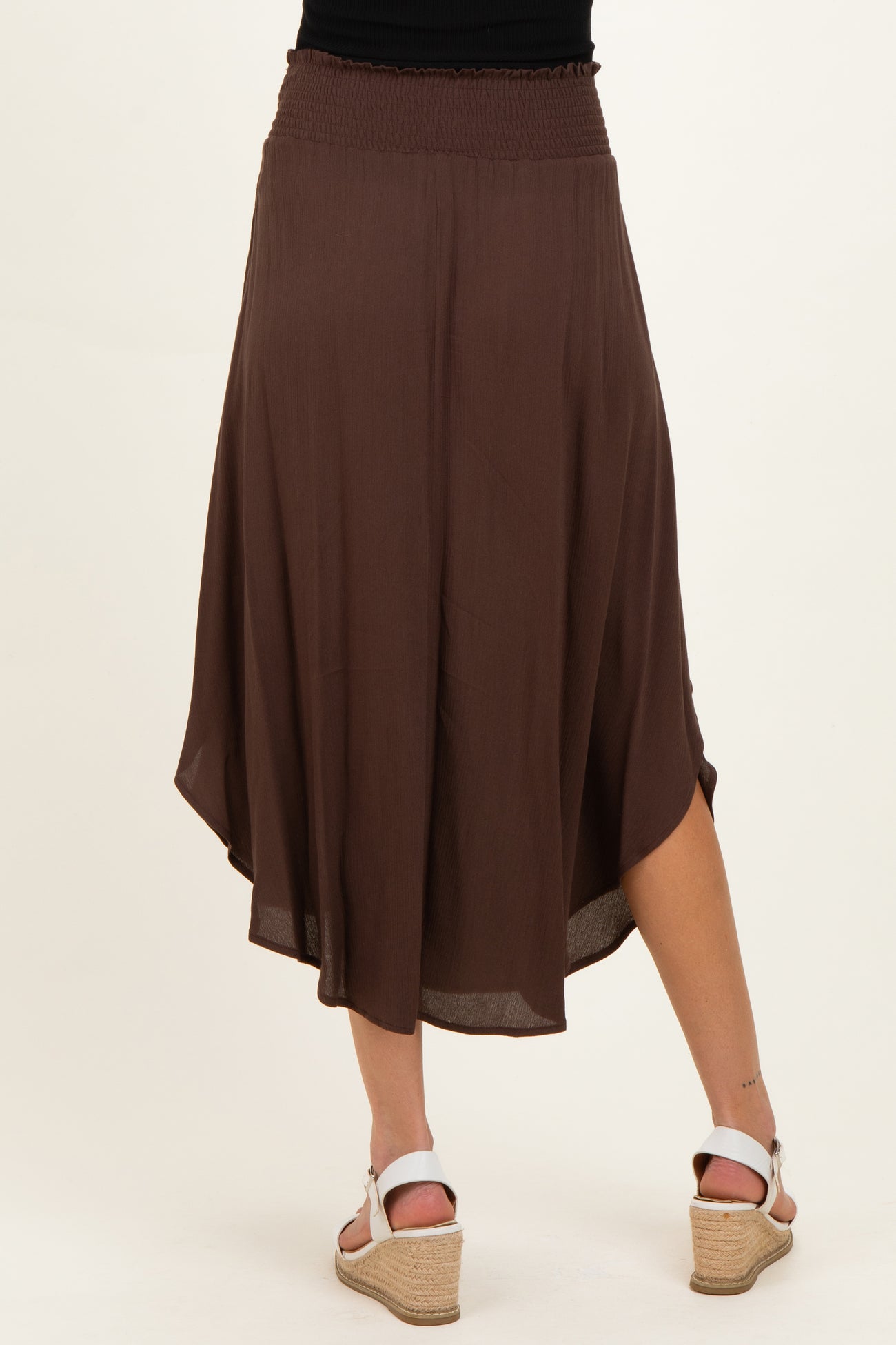 woman wearing a brown maternity skirt with an asymmetrical hem and a smocked waistband, seen from the back