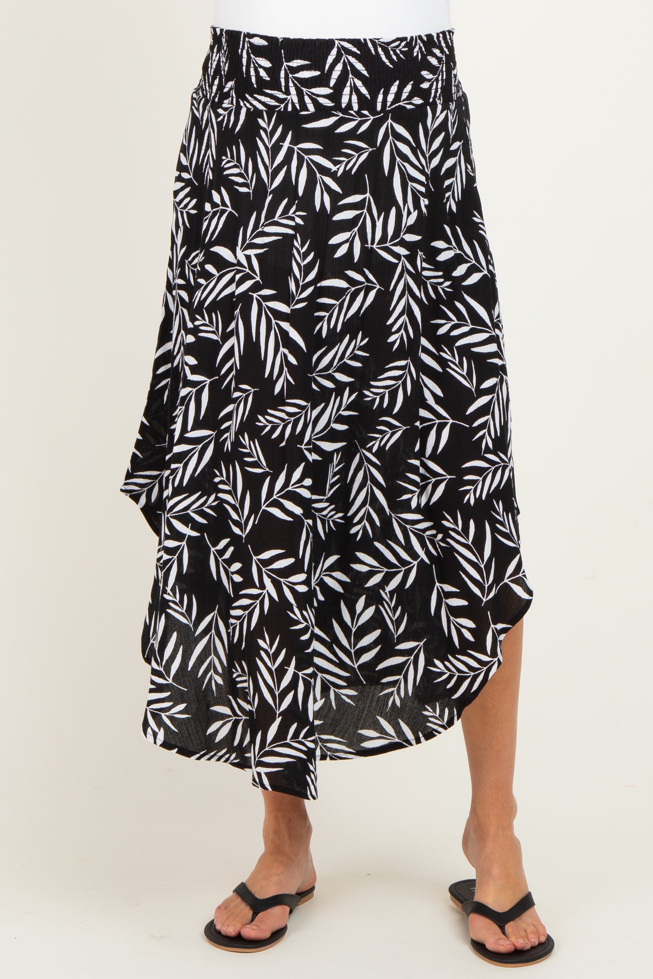 maternity wear black and white leaf print wrap skirt with an asymmetrical hem, model wearing it with flip-flops
