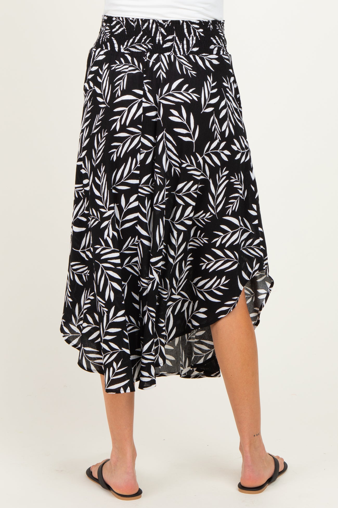 woman wearing a black midi maternity skirt with white leaf print and asymmetrical hem, showing her back