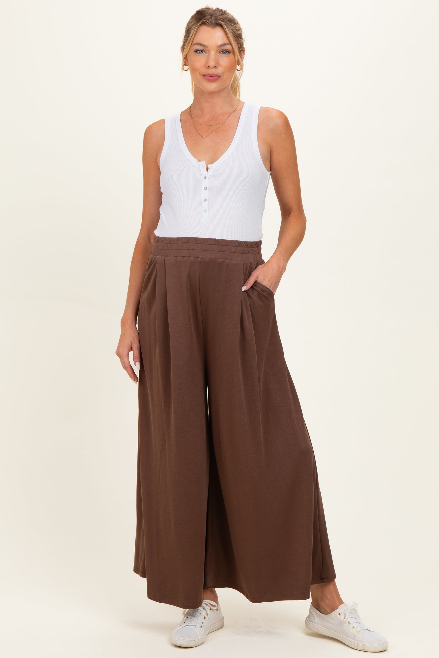woman wearing a light brown maternity wide leg pants with pockets and a white sleeveless top