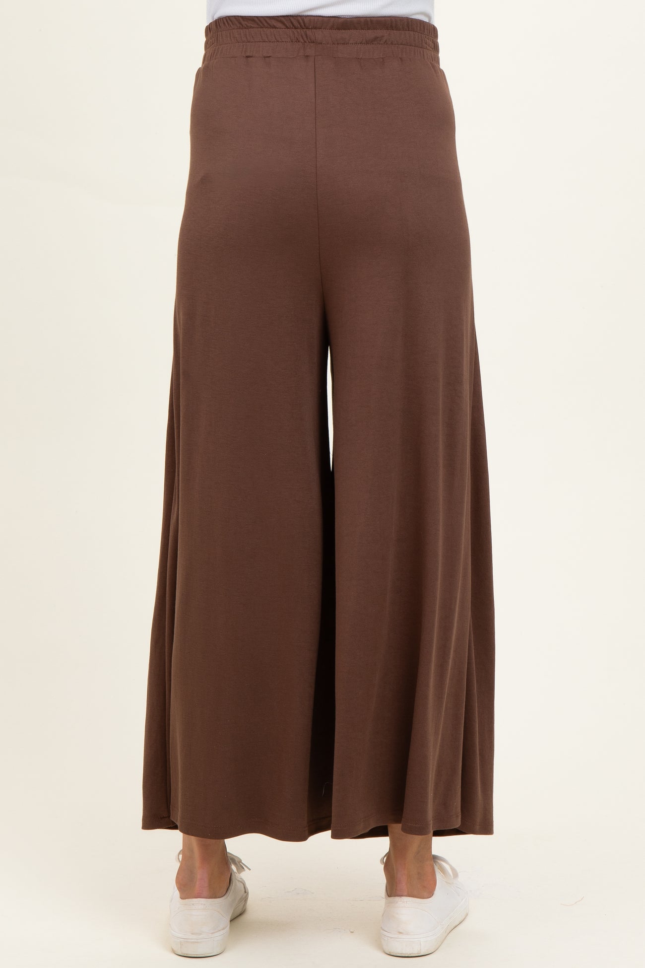 woman wearing brown wide-leg maternity pants, showing the back view and styled with white sneakers