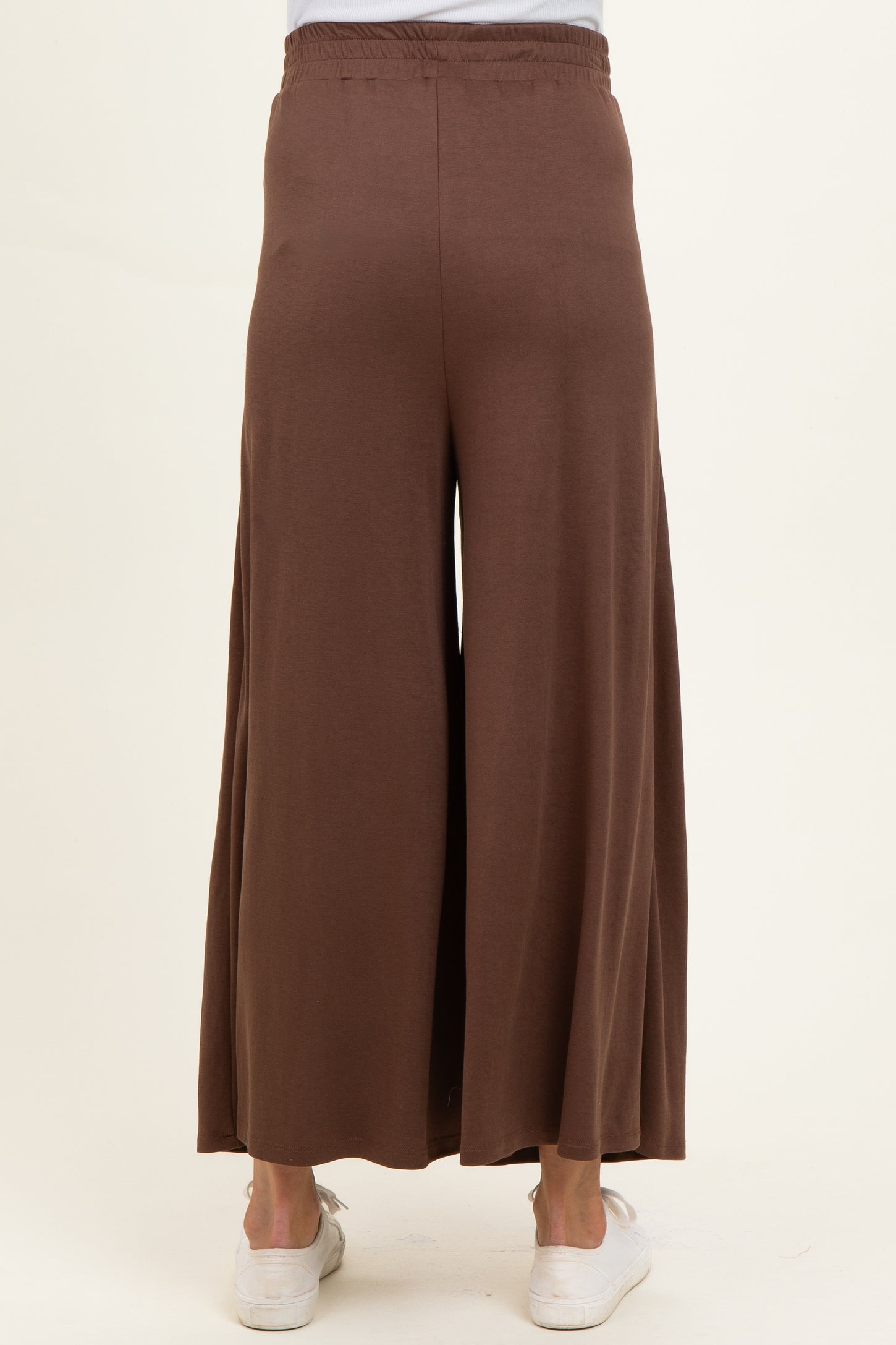 woman wearing brown wide-leg maternity pants, showing the back view and styled with white sneakers