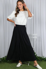 woman wearing a white short sleeve blouse with ruffles and a black wide-leg maxi skirt