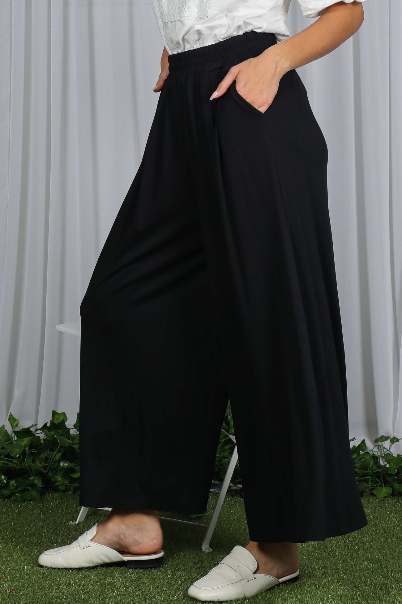 woman wearing black wide-leg pants with elastic waistband and side pockets, styled casually with white slippers