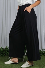 woman wearing black wide-leg pants with elastic waistband and side pockets, styled casually with white slippers