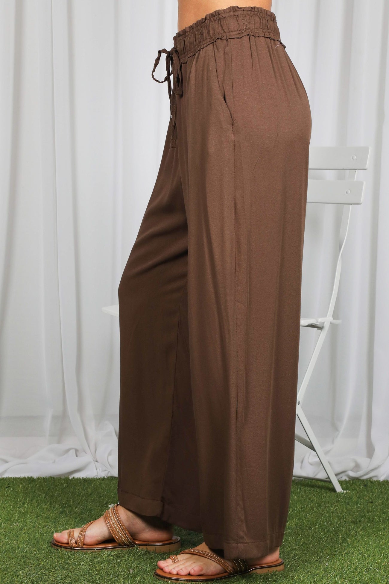 woman wearing brown wide-leg pants with an elastic waistband and drawstring, styled with sandals