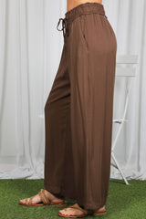 woman wearing brown wide-leg pants with an elastic waistband and drawstring, styled with sandals