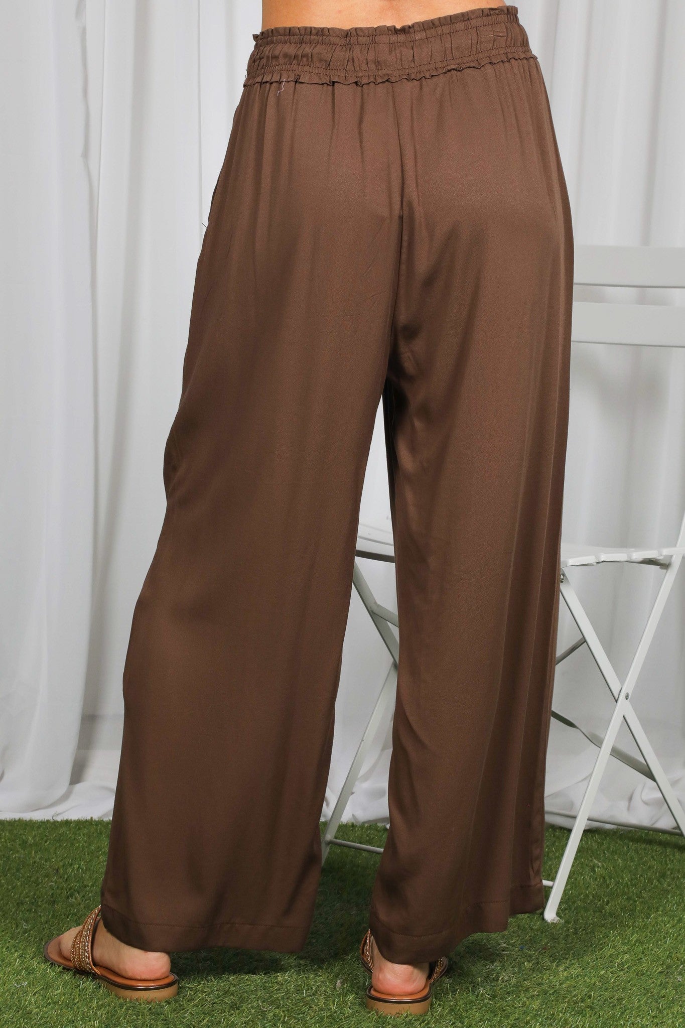 woman wearing brown wide-leg pants with an elastic waistband, shown from the back on a grassy surface