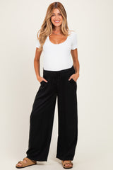 woman wearing a white short sleeve maternity top and black wide-leg maternity pants, holding her baby bump