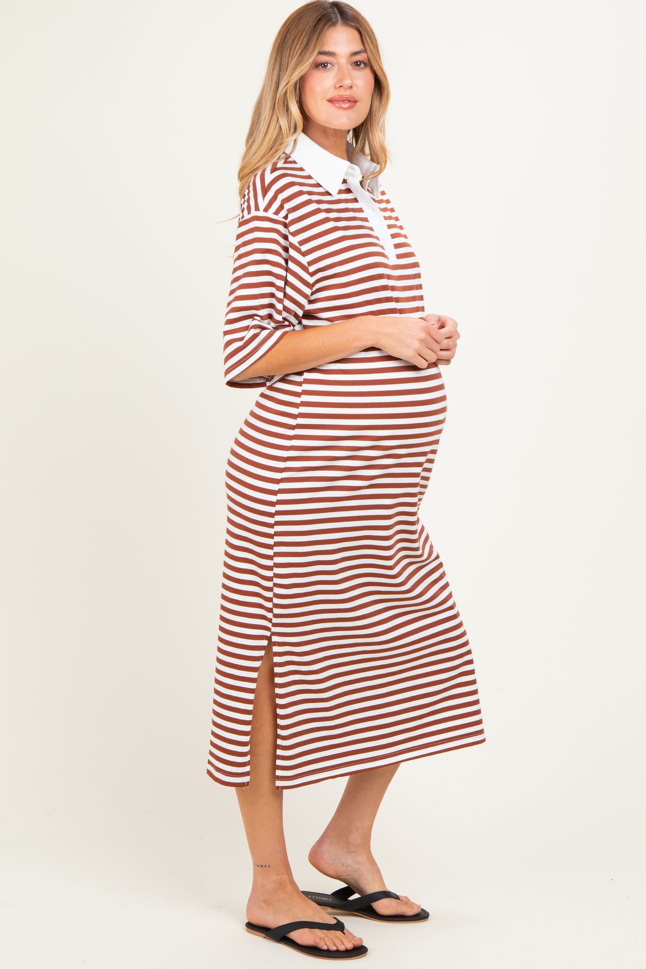 woman wearing a brown and white striped maternity dress with a collared neckline and side slits, showing her baby bump