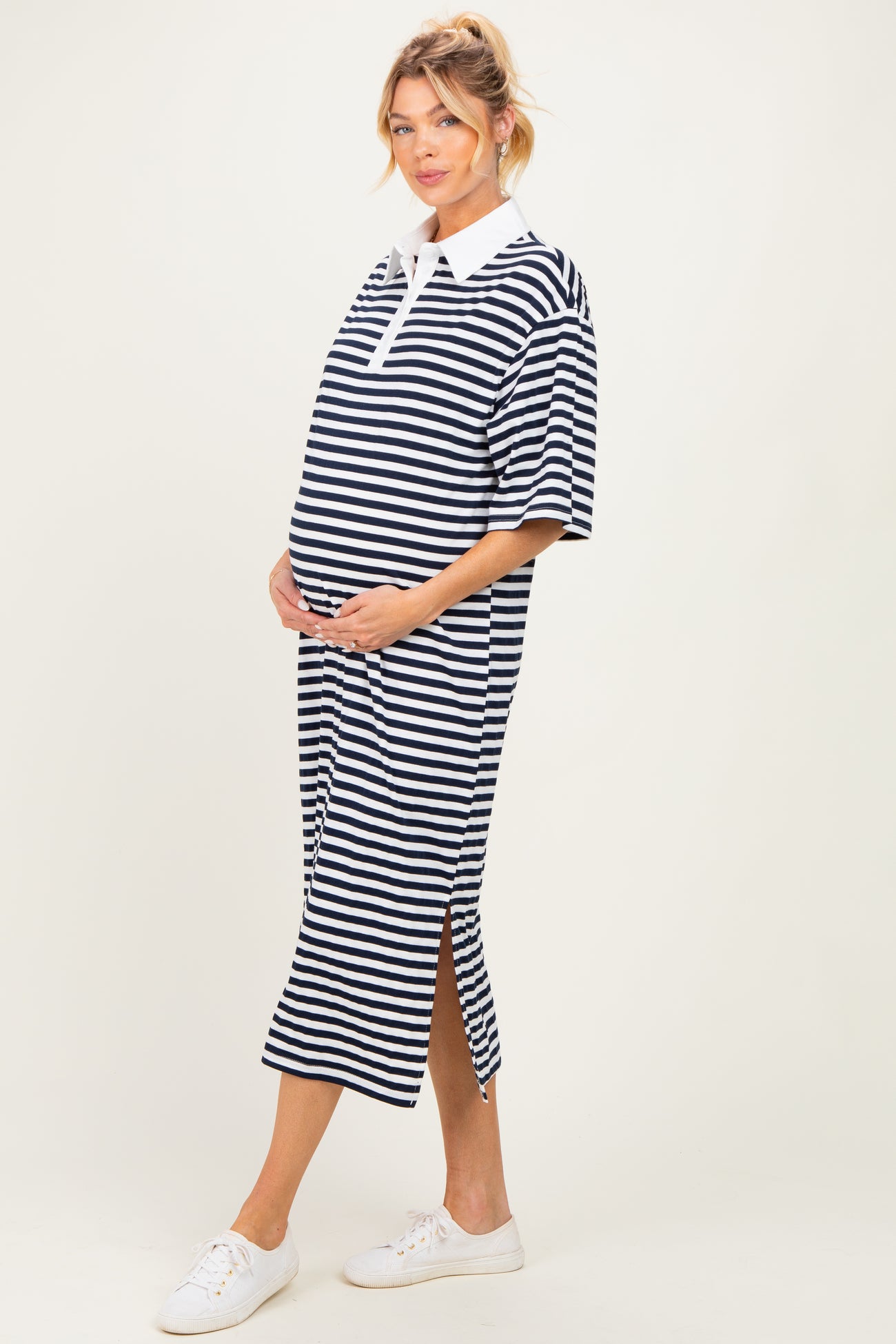 woman wearing a black and white striped maternity polo dress with a side split, gently cradling her baby bump