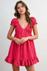 woman wearing a pink short puff sleeve dress with a smocked bodice and ruffle hem, featuring front buttons
