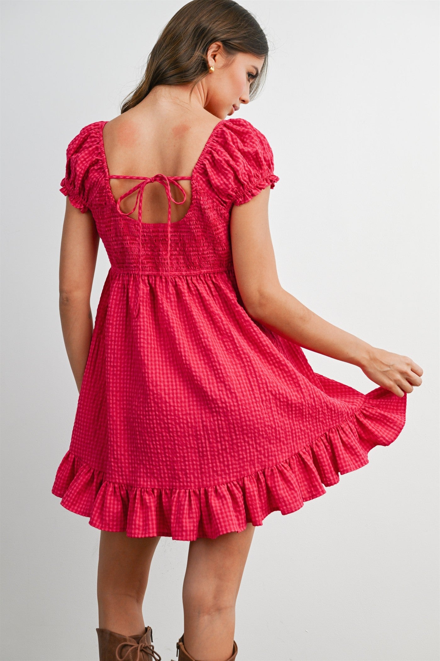 woman wearing a pink short dress with puff sleeves and a ruffled hem, showing a tie-back detail