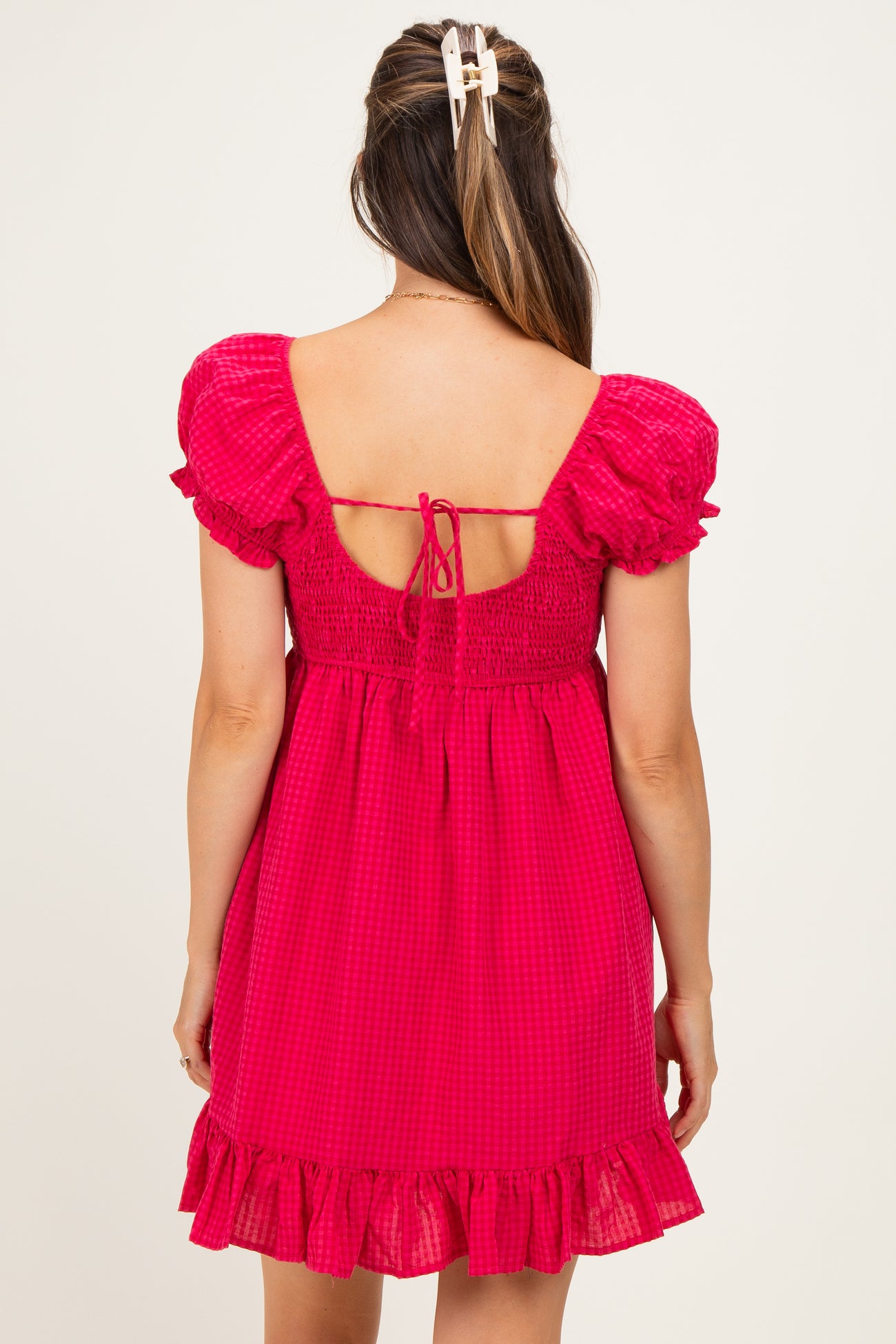 woman wearing a fuchsia checkered maternity dress with puff sleeves and a ruffled hem, showing off a baby bump from the back