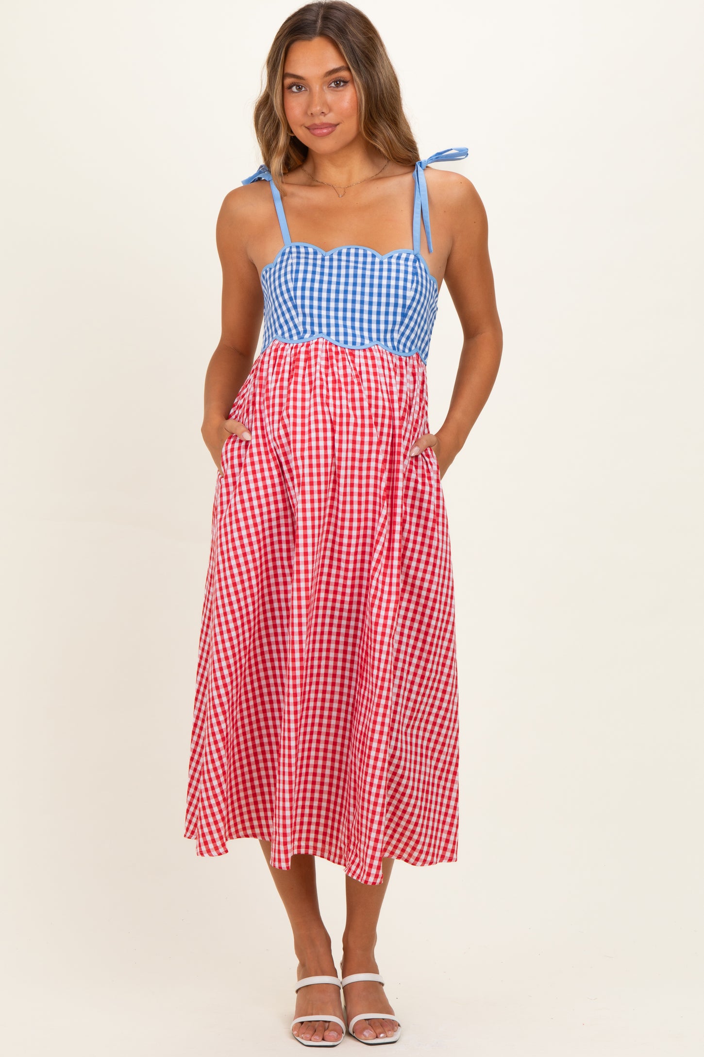 woman wearing a blue and red gingham maternity dress with adjustable straps and pockets