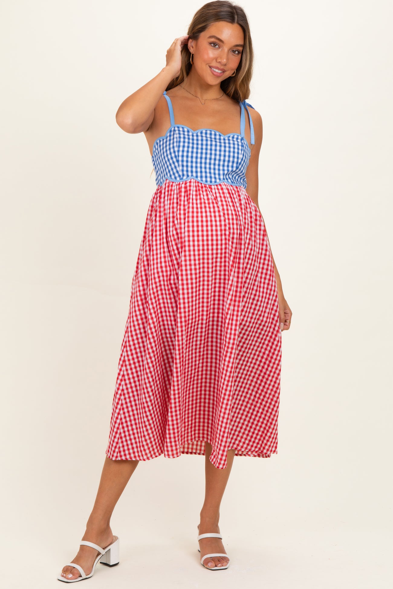 woman wearing a blue and red gingham maternity dress with a fitted bodice and flowing skirt, showing her baby bump
