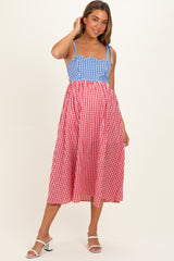 woman wearing a blue and red gingham maternity dress with a fitted bodice and flowing skirt, showing her baby bump