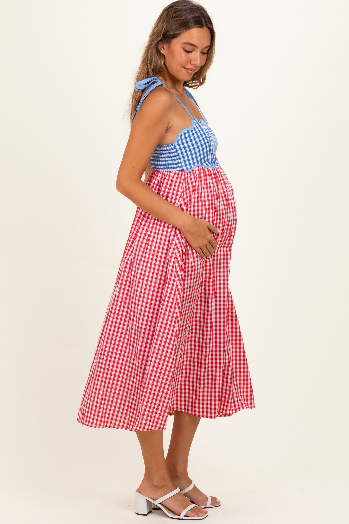 woman wearing a blue and red gingham maternity dress with a fitted bodice and flowing skirt, showing her baby bump