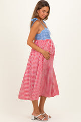 woman wearing a blue and red gingham maternity dress with a fitted bodice and flowing skirt, showing her baby bump