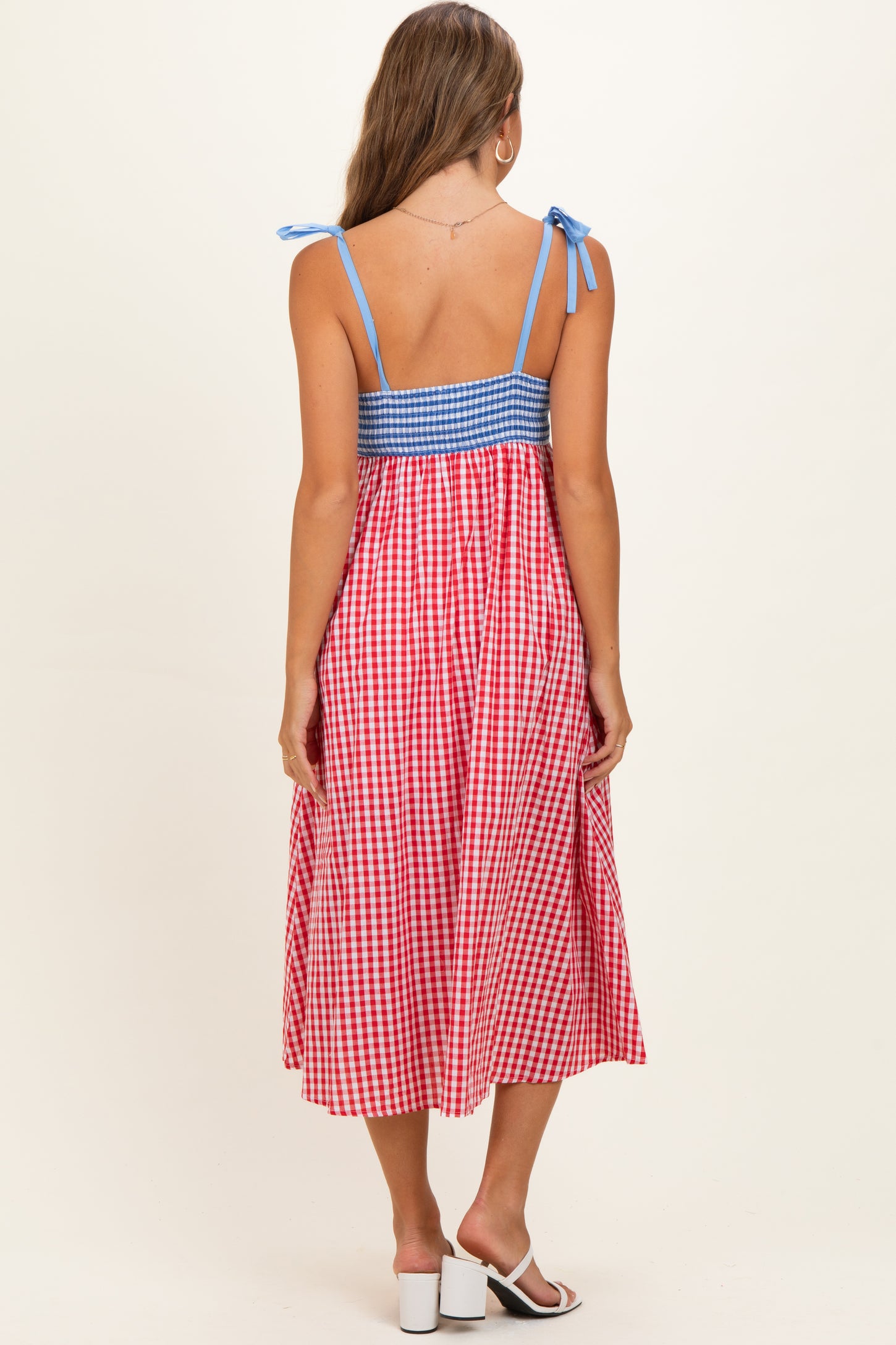 woman wearing a red and white gingham maternity dress with blue checkered bodice and shoulder ties, showing back view