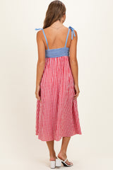 woman wearing a red and white gingham maternity dress with blue checkered bodice and shoulder ties, showing back view