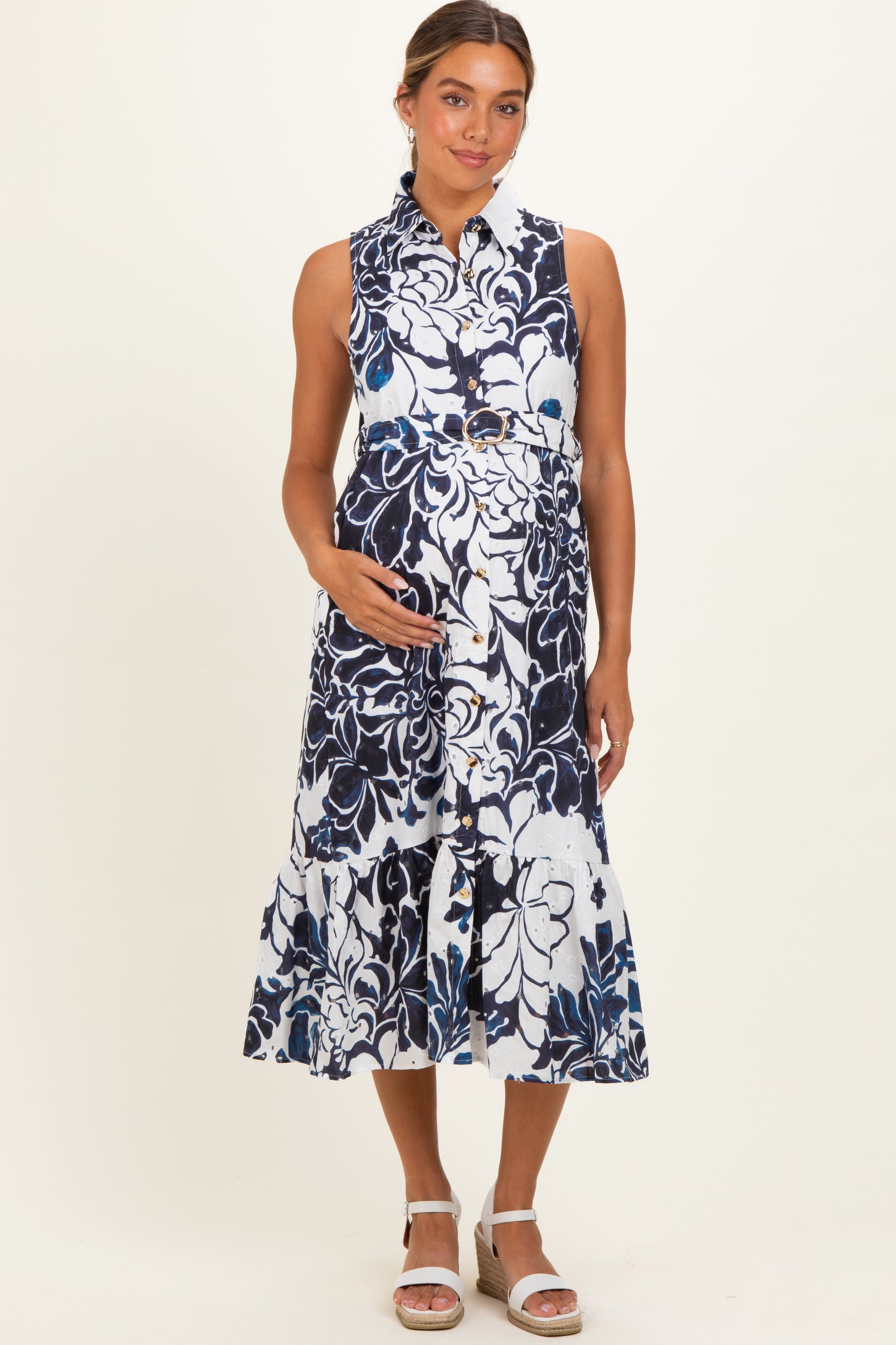 woman wearing a navy and white floral maternity dress with a button front and ruffle hem, holding her baby bump