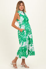 woman wearing a green floral print maternity dress with sleeveless design and a flared hem, showing baby bump