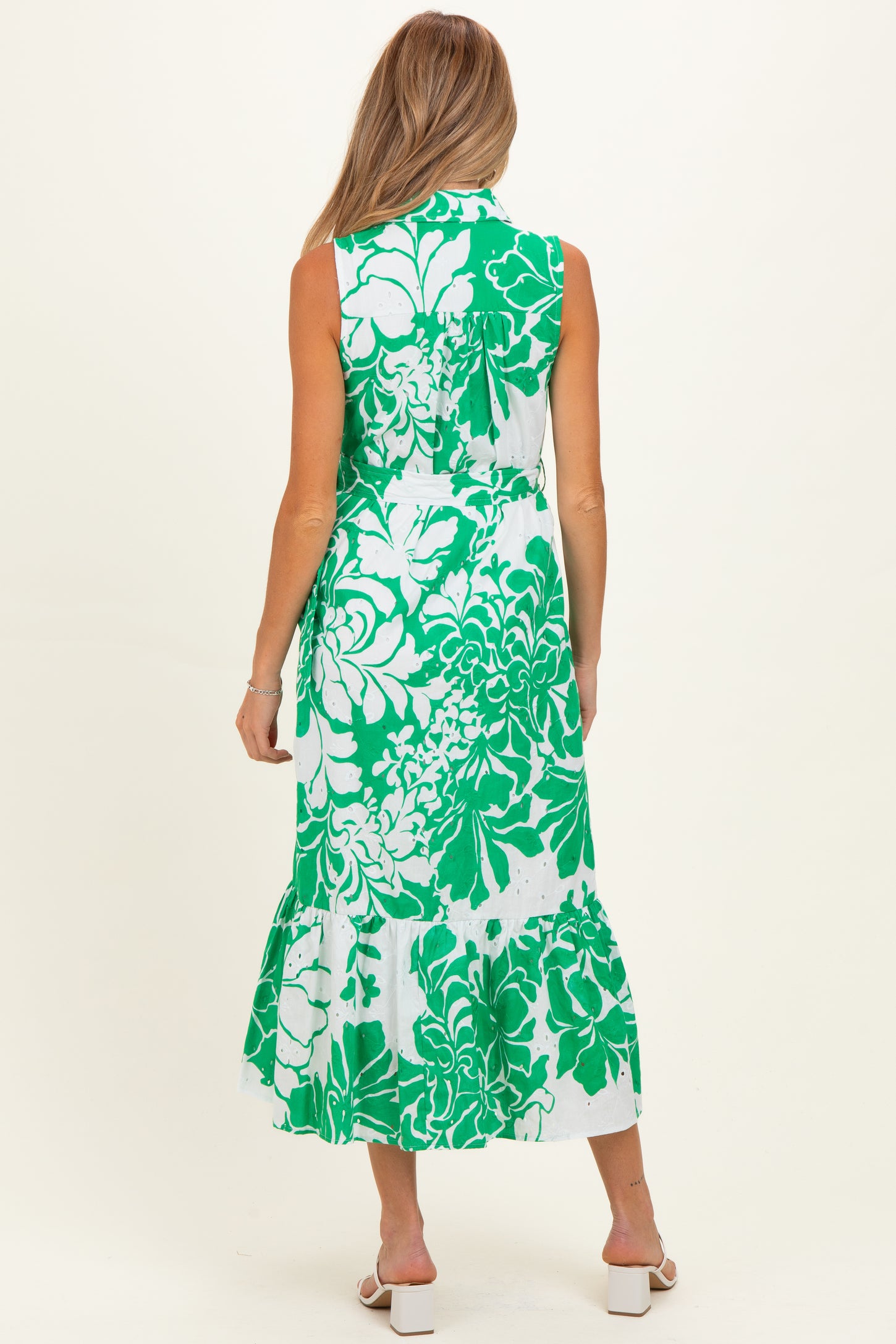 woman wearing a sleeveless green and white floral maternity dress with a flared hemline and back tie detail