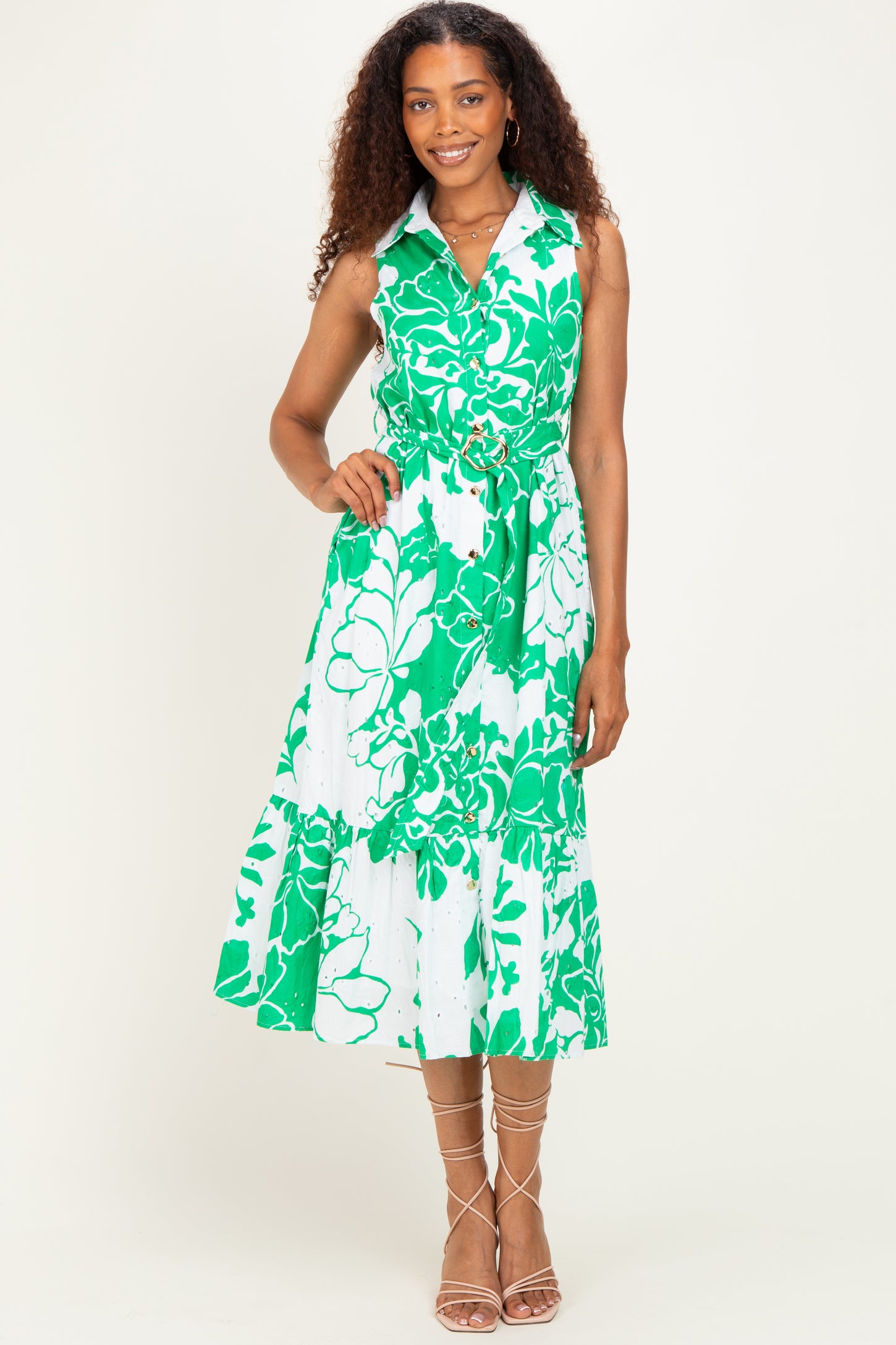 woman wearing a white dress with green floral print, featuring a collar and a tie waist, standing against a plain background