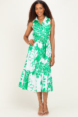 woman wearing a white dress with green floral print, featuring a collar and a tie waist, standing against a plain background