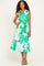 woman wearing a white dress with green floral print, featuring a collar and a tie waist, standing against a plain background