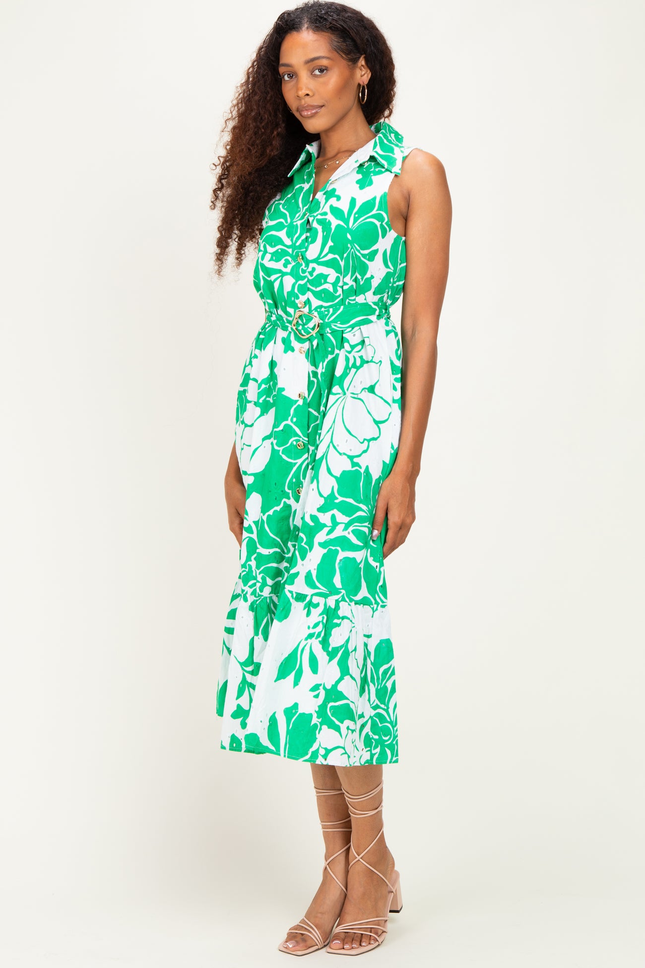 woman wearing a sleeveless green and white floral maxi dress with a belted waist and strappy sandals