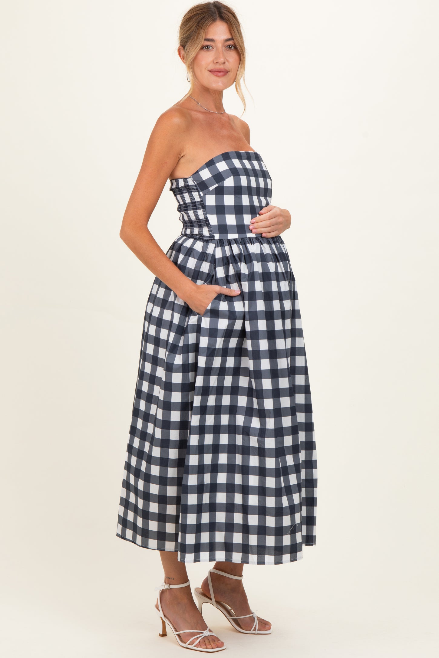 woman wearing a navy and white gingham strapless maternity dress with pockets and a visible baby bump
