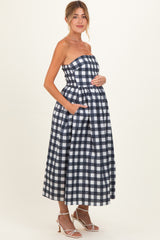 woman wearing a navy and white gingham strapless maternity dress with pockets and a visible baby bump