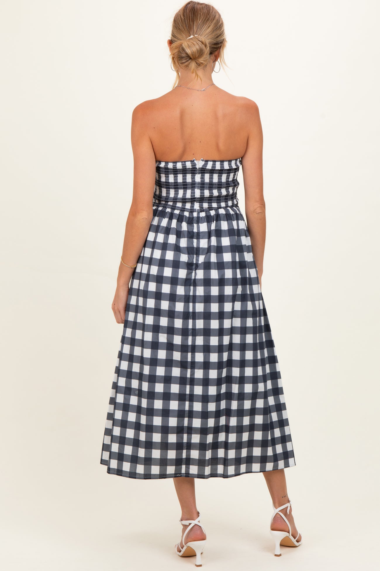 woman wearing a navy and white gingham strapless maternity dress with a smocked bodice and a flowy skirt