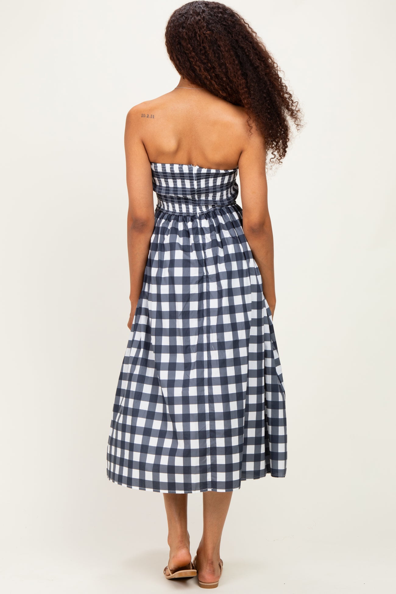 woman wearing a navy and white checkered strapless maxi dress, showing the back view with elastic waist and full skirt