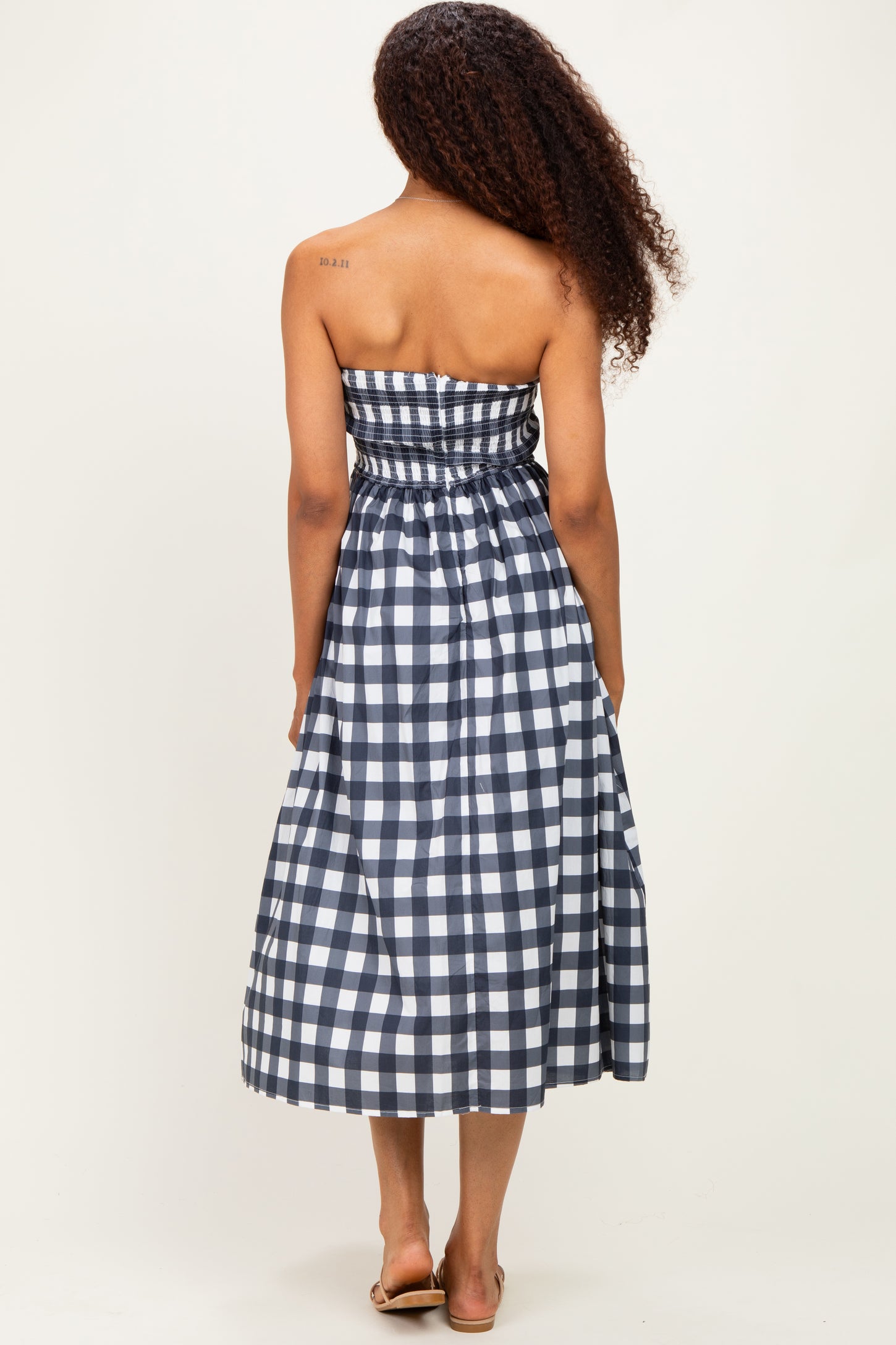woman wearing a navy and white checkered strapless maxi dress, showing the back view with elastic waist and full skirt