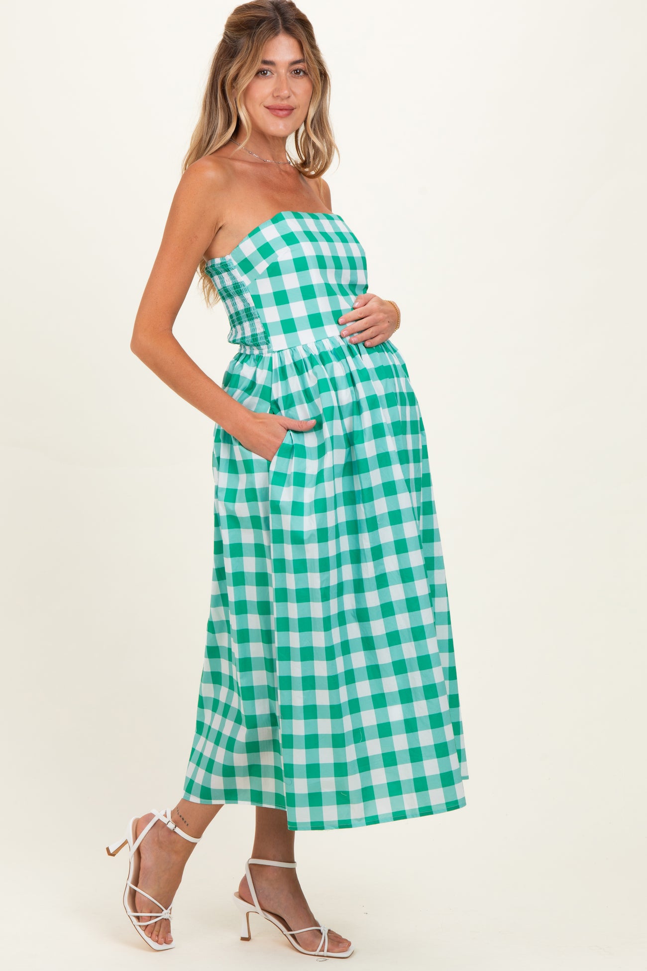 woman wearing a green and white checkered maternity dress with a strapless design and side pockets, baby bump visible