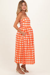 woman wearing an orange and white checkered strapless maternity dress with a fitted bodice and pockets