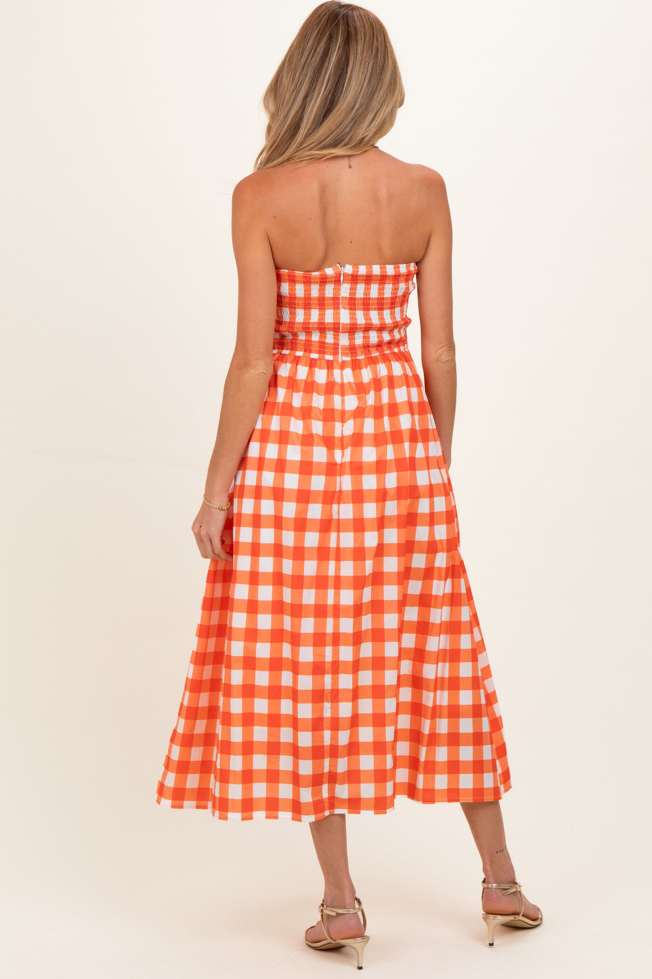 woman wearing an orange and white gingham strapless maternity dress with a smocked bodice and flowing skirt