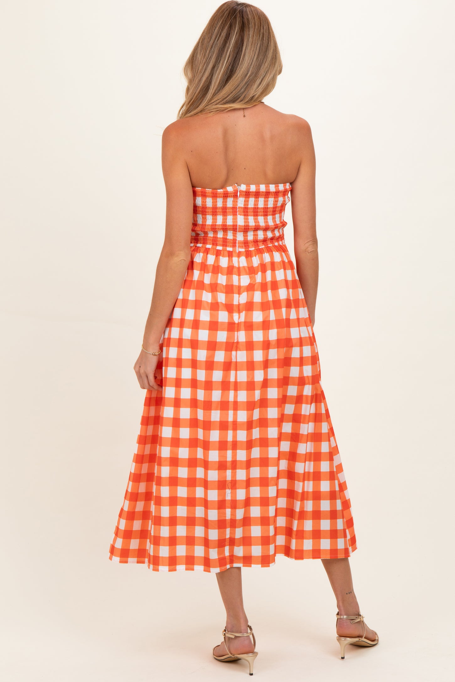 woman wearing an orange and white gingham strapless maternity dress with a smocked bodice and flowing skirt