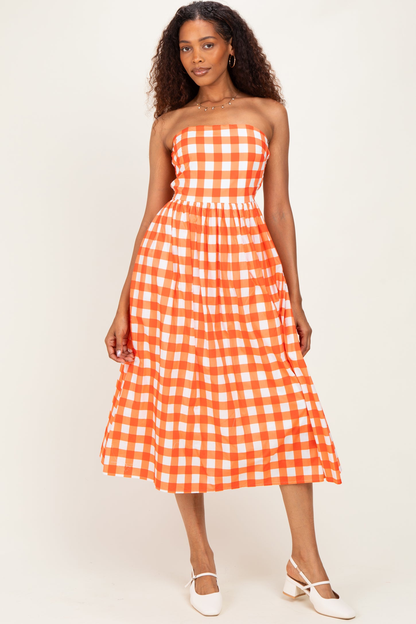 woman wearing an orange and white checkered strapless midi dress with a fitted bodice and flowy skirt