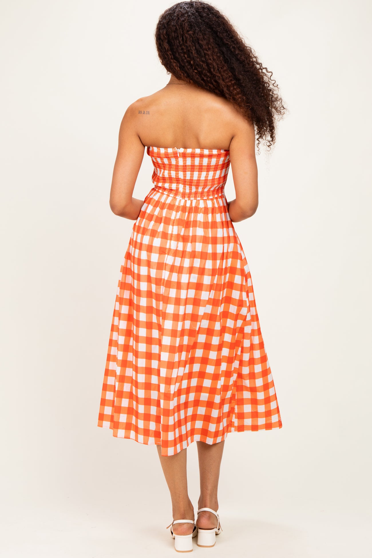woman wearing an orange and white checkered strapless midi dress, showing the back view and curly hair
