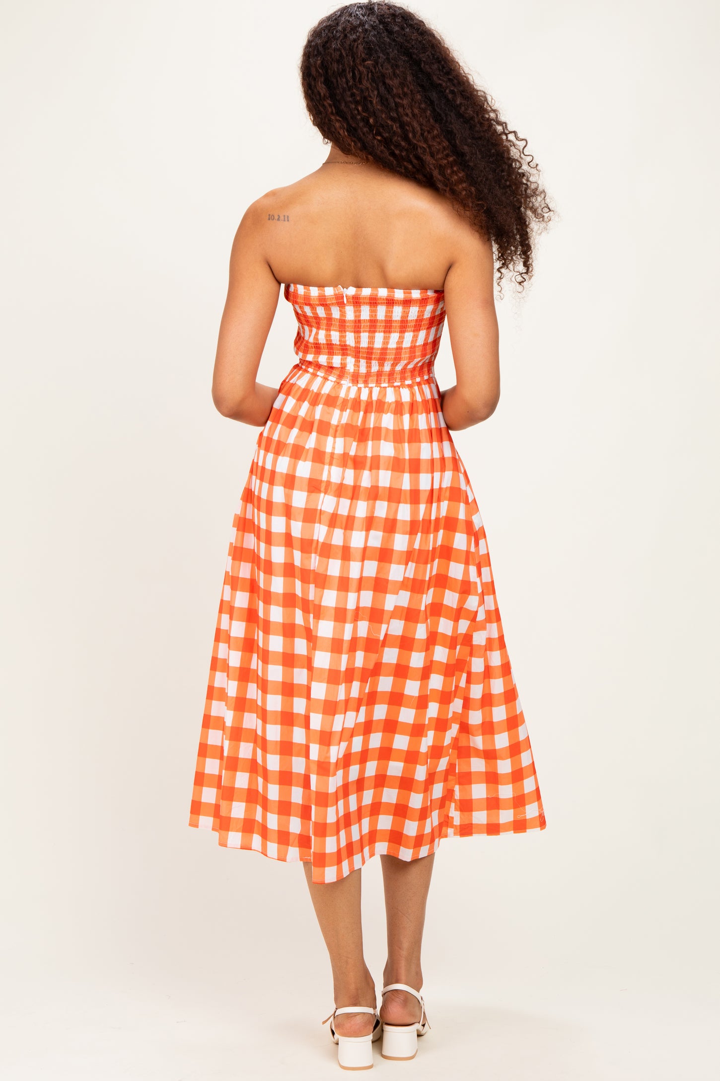 woman wearing an orange and white checkered strapless midi dress, showing the back view and curly hair
